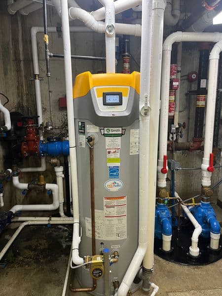 Modern water heater with digital display in utility room, surrounded by plumbing infrastructure.