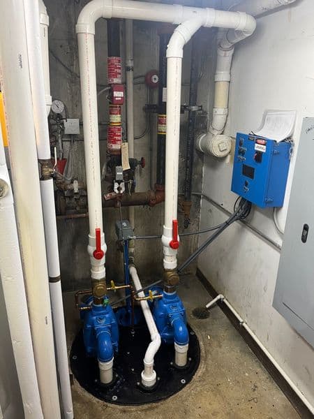 Blue sump pumps with white piping in a basement utility room.