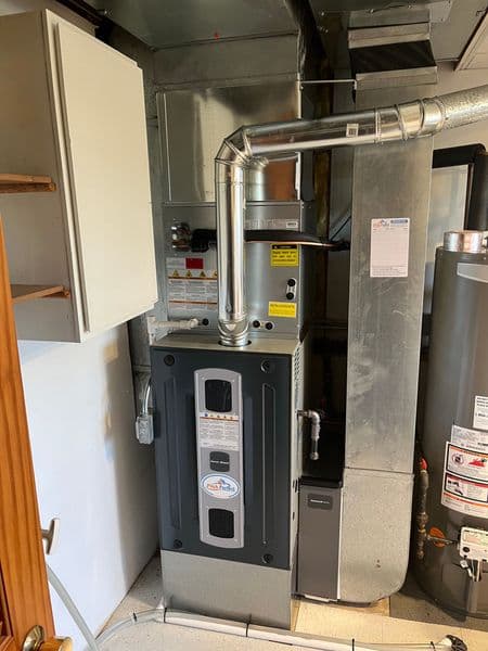 Furnace with venting pipe and adjacent water heater in a utility room setting.