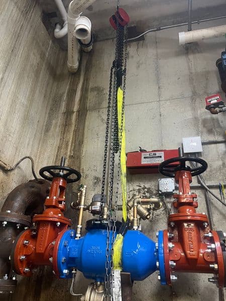 Red and blue industrial valves with chains and a hoist in a concrete facility setting.