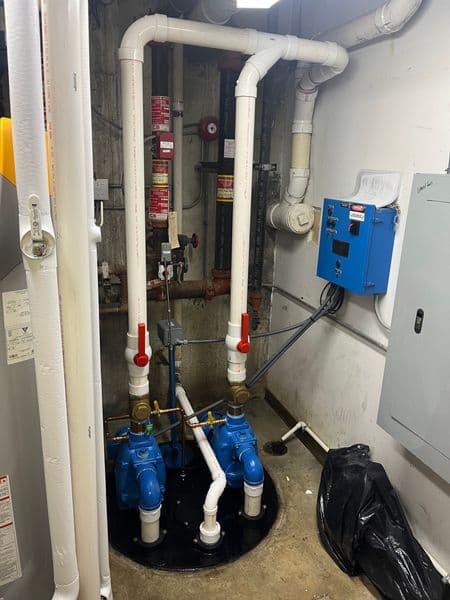 Blue sump pumps with white PVC pipes in a building basement utility room.