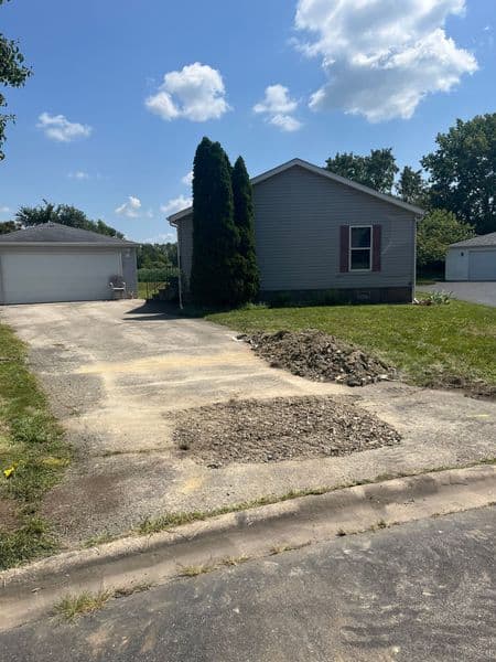Residential property with driveway undergoing maintenance and gravel pile, green grass, and cloudy sky.