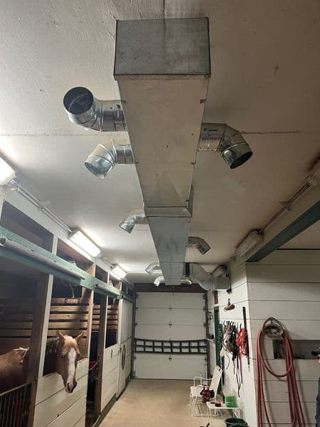 Metal ductwork installed in a barn, providing ventilation for horses in nearby stalls.