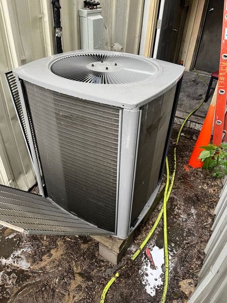 Air conditioning unit near building entrance, with visible water damage and hose attached.