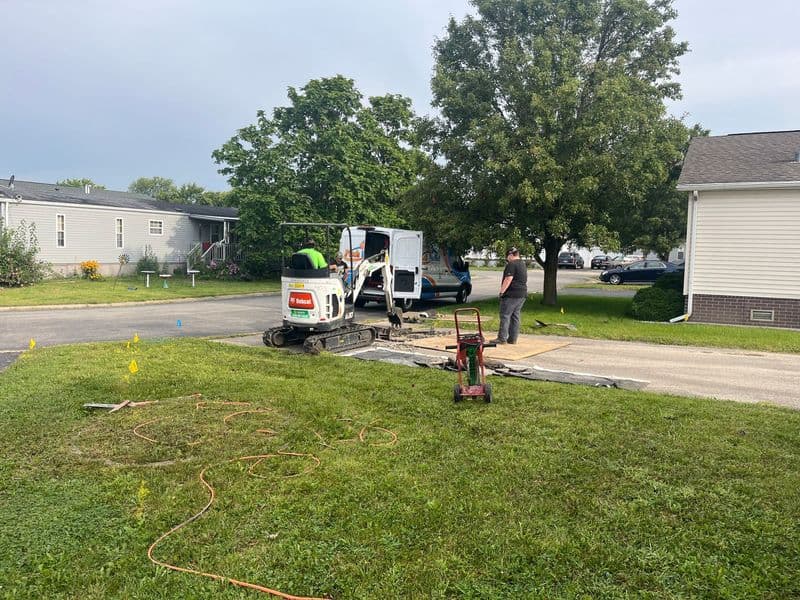 Construction workers using equipment on a residential driveway for repairs and maintenance.