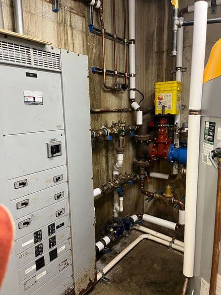 Utility room with electrical panel and various pipes and valves, showing plumbing system details.